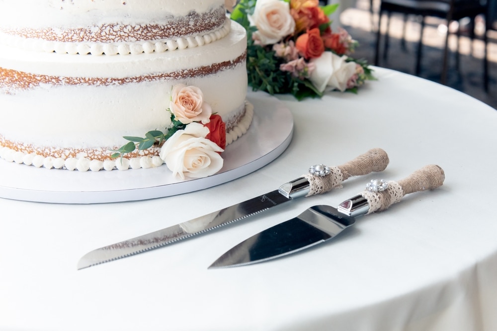 Wedding cake adorned with roses in Minnesota Fall Colors on table, next to silver serving utensil ready for cake cutting at Water Street Inn, one of the best Stillwater Wedding Venues.